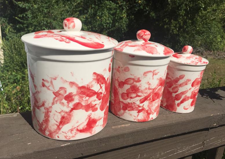 Three white kitchen canisters splattered with red handprints